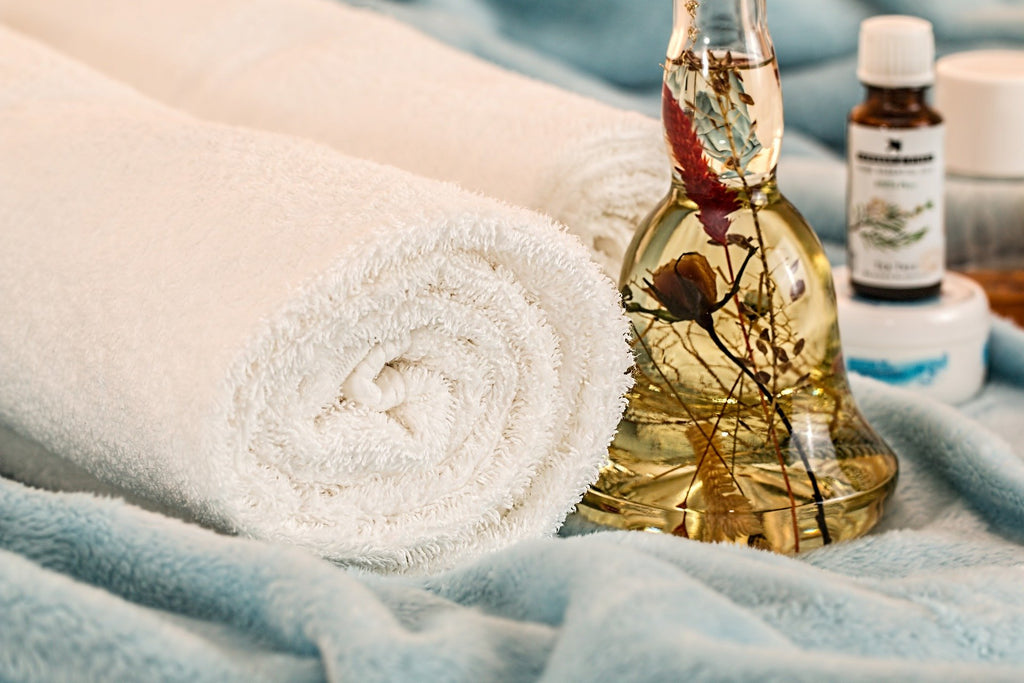 Image of carrier oil infused with essential oils and two towels in a spa like setting